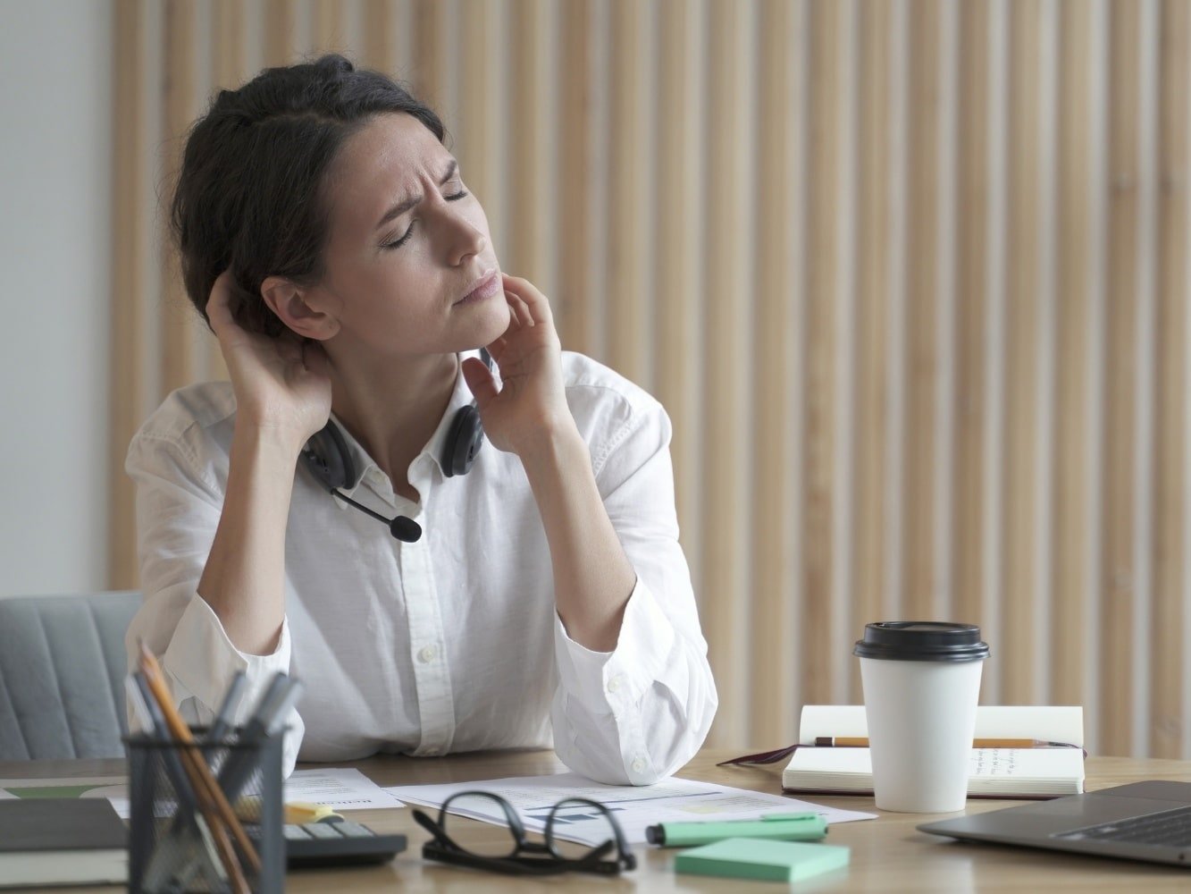 Frau am Schreibtisch mit Muskelrheumatismus und Stress