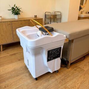 Mobiele Headspa unit in wit met gouden kraan naast een behandelbed in een spa-ruimte